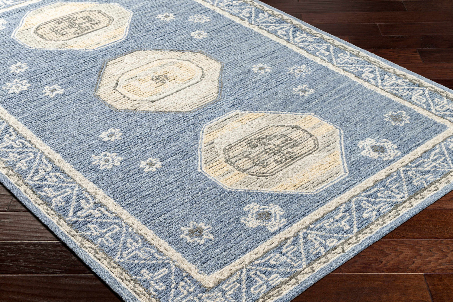Close-up of the hand-tufted Arwan Area Rug. Farmhouse style with beige, gray, and blue floral and geometric patterns. Corner