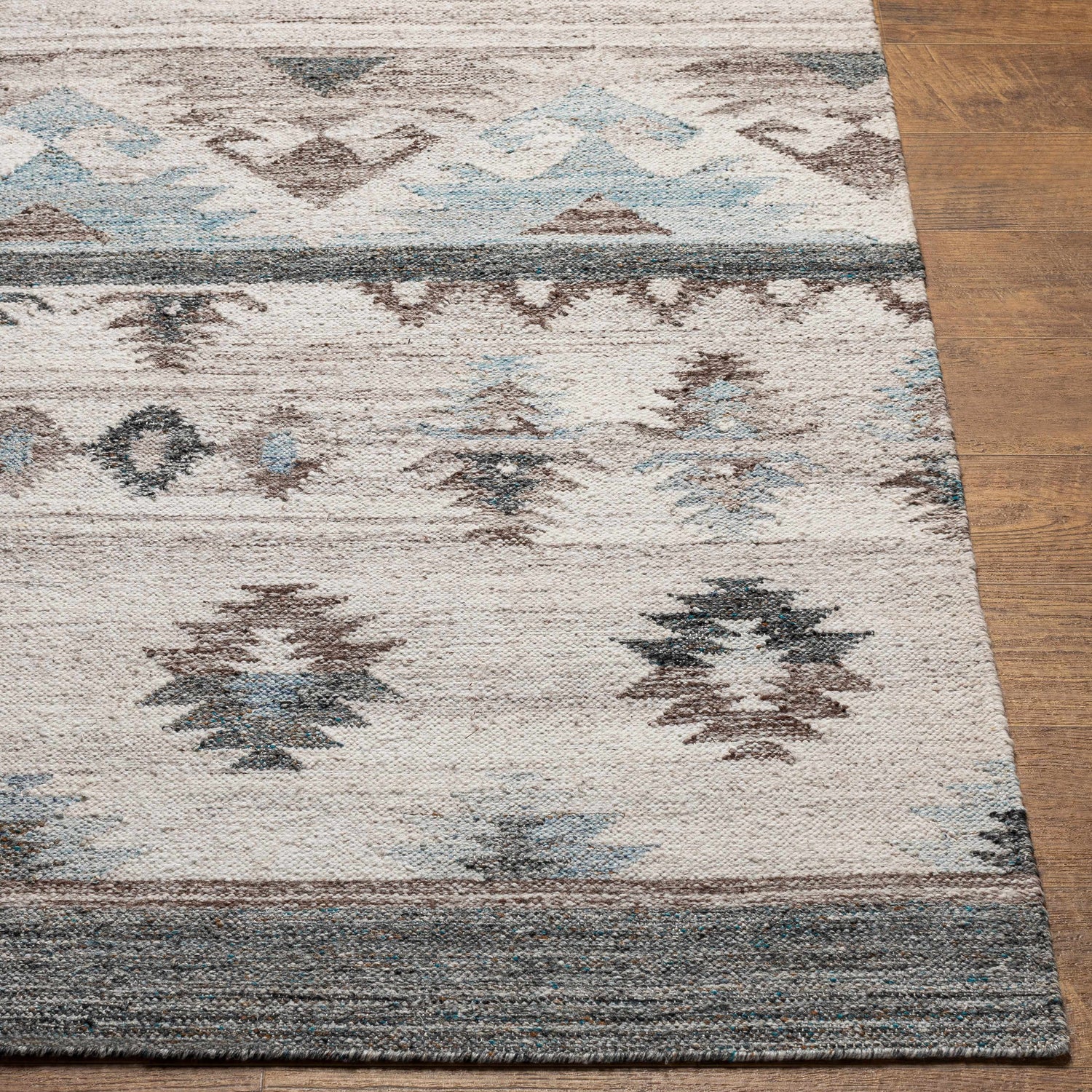 Close-up of the hand-woven Duyen Area Rug. Features a Southwestern design in black, blue, brown, and white recycled PET yarn. Front