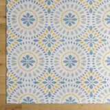 Close-up of the Karin Area Rug, a light gray rug with a coastal-inspired blue, gold, and gray floral medallion pattern. Corner