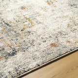 Close-up of the Kacia Area Rug showing beige, bone, gold, and navy abstract pattern and soft polyester texture. Texture
