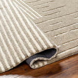 Close-up of the Akuji Area Rug showing its hand-tufted wool texture and geometric striped pattern in light peach and brown. Fold