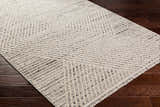 Close-up of Brita Area Rug in bone and cloud gray with a geometric pattern on dark brown wood floors. Corner