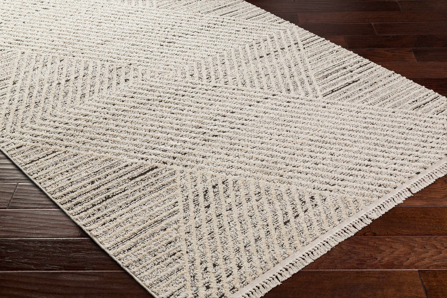 Close-up of Brita Area Rug in bone and cloud gray with a geometric pattern on dark brown wood floors. Corner