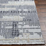 Close up of Bodhi Textured Saxony Rug. Gray, light gray, and charcoal hues with a geometric pattern and soft fringes. Front