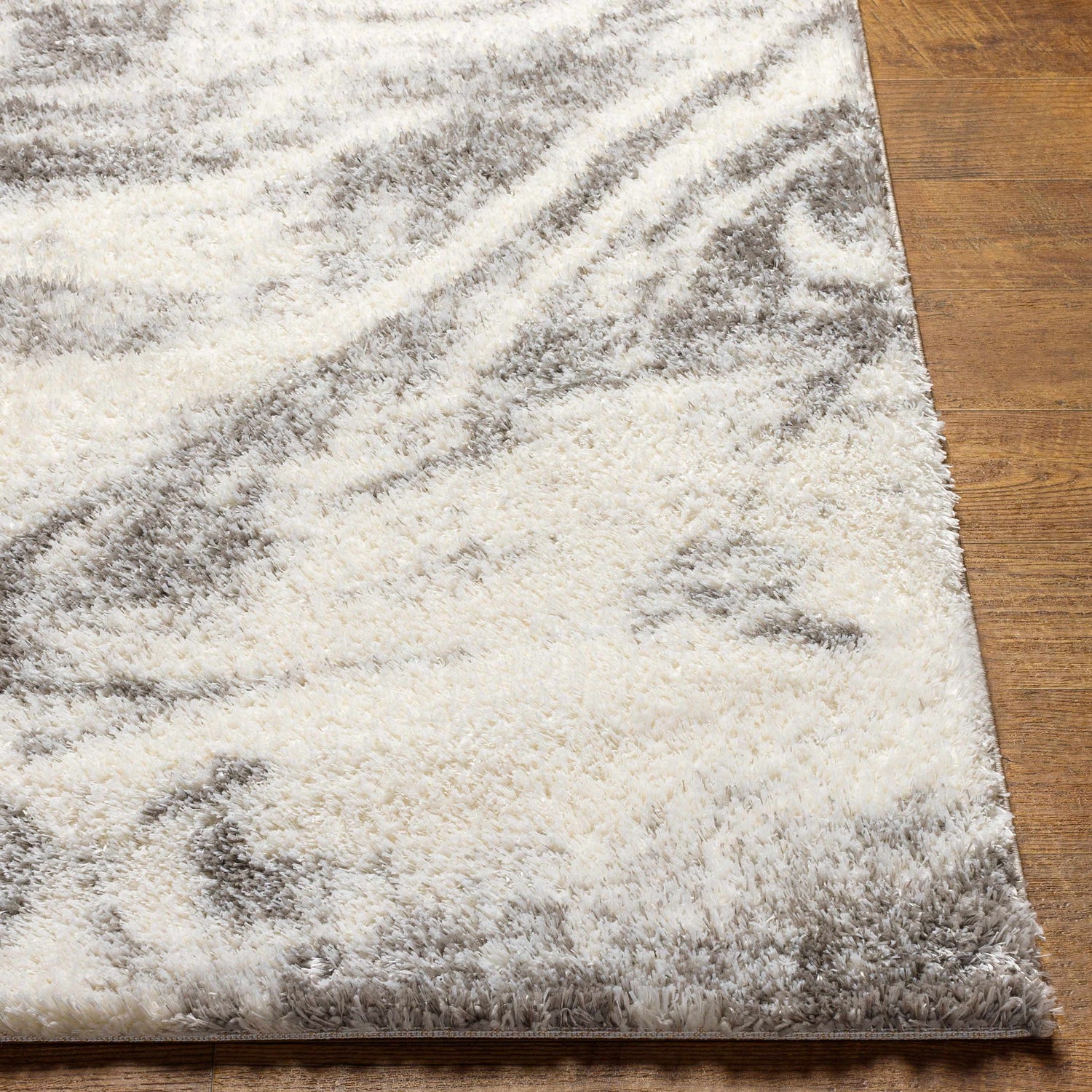 Close up of the Delma Area Rug showing its shag texture and cloud gray, off white, and smoke color palette. Front