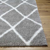 Close-up of the Faye Area Rug, a gray shag rug with a white geometric diamond pattern on light wood flooring. Front