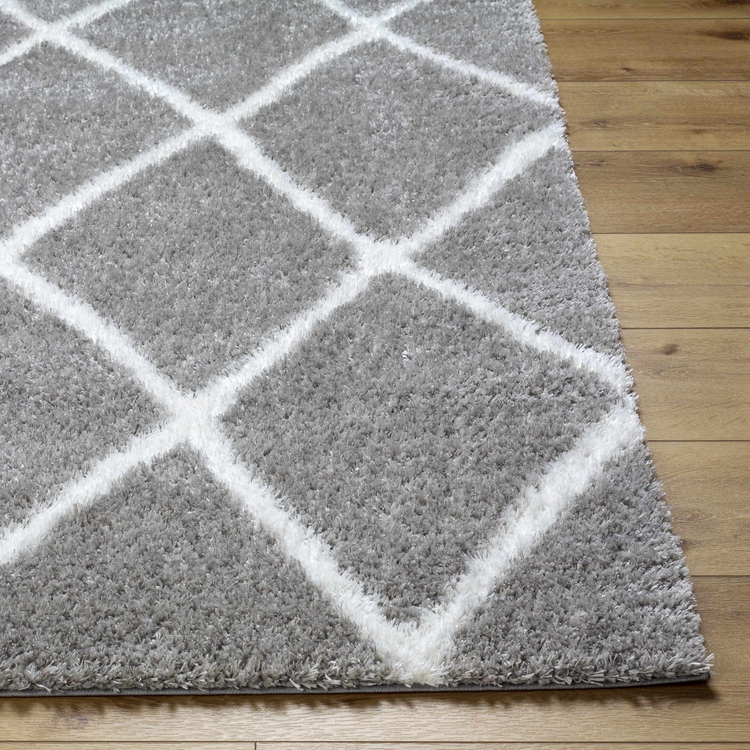 Close-up of the Faye Area Rug, a gray shag rug with a white geometric diamond pattern on light wood flooring. Front