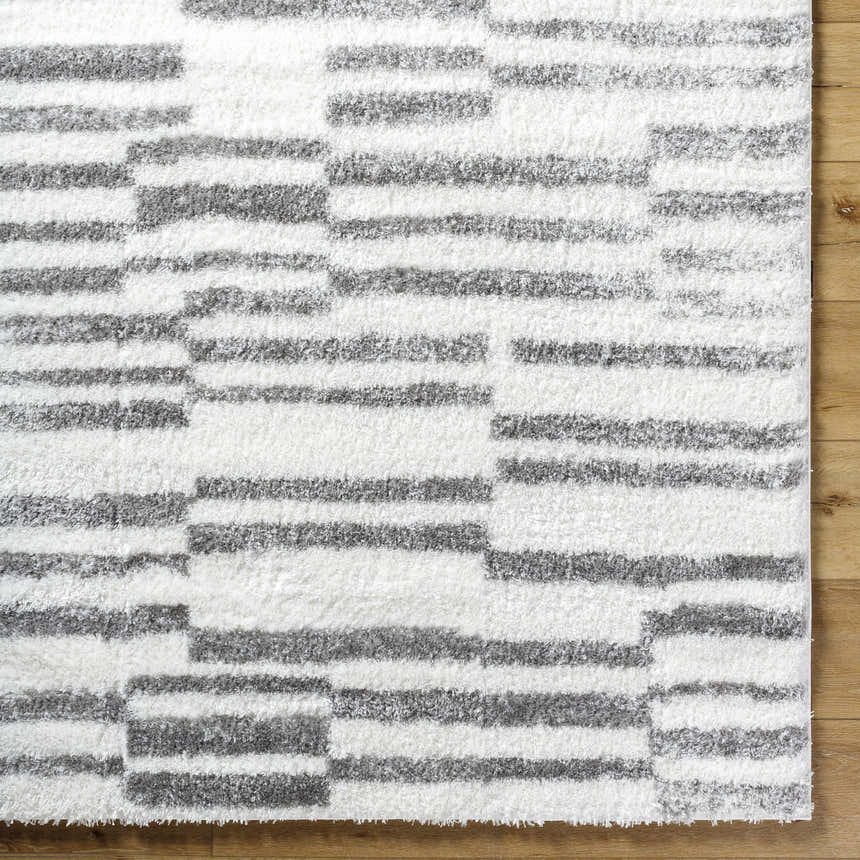 Close-up of the Kuron Area Rug showing its charcoal and off-white shag stripes and soft, textured pile. Corner