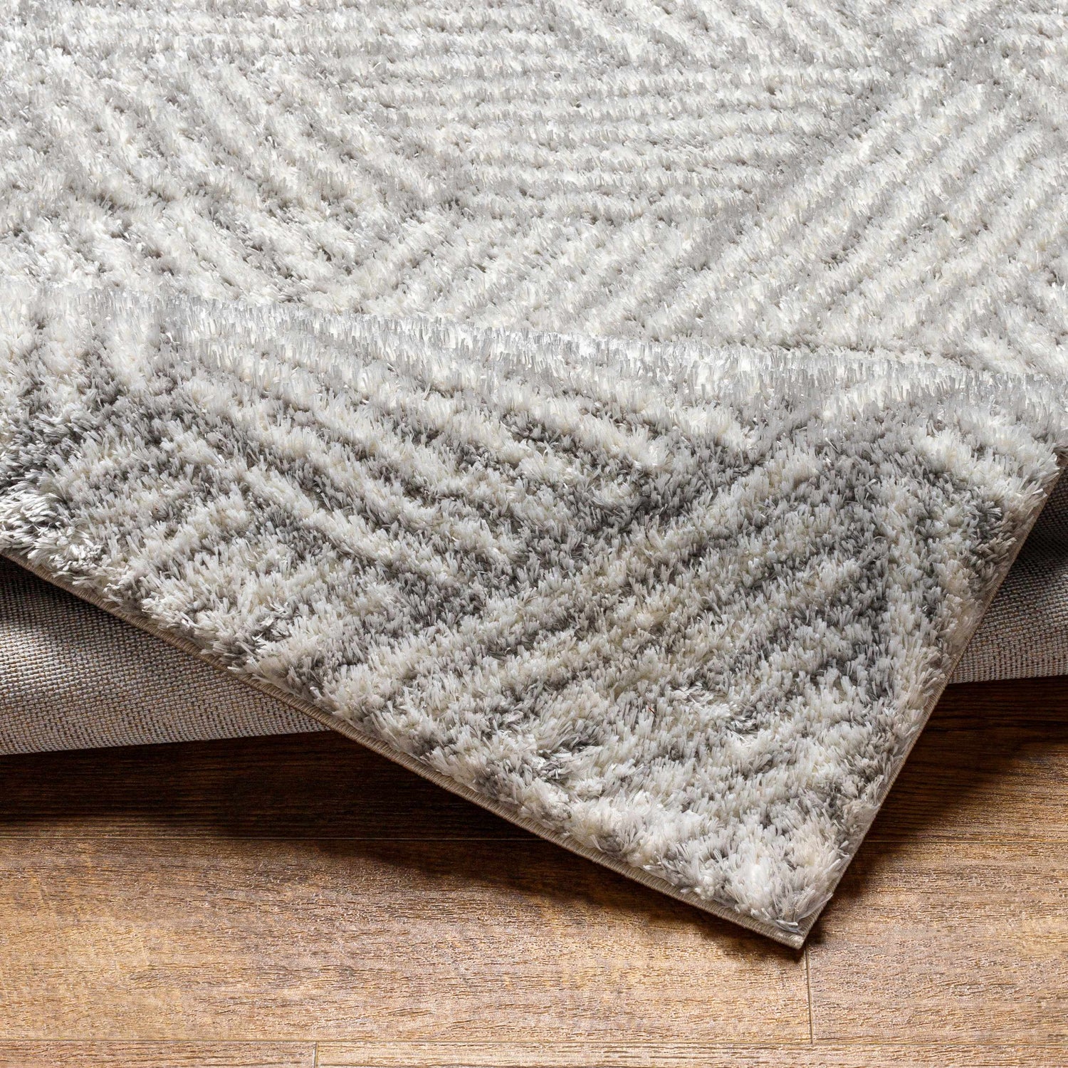 Close-up of the Mura Gray Area Rug showing its shag texture and geometric pattern in beige, gray, and off-white. Fold