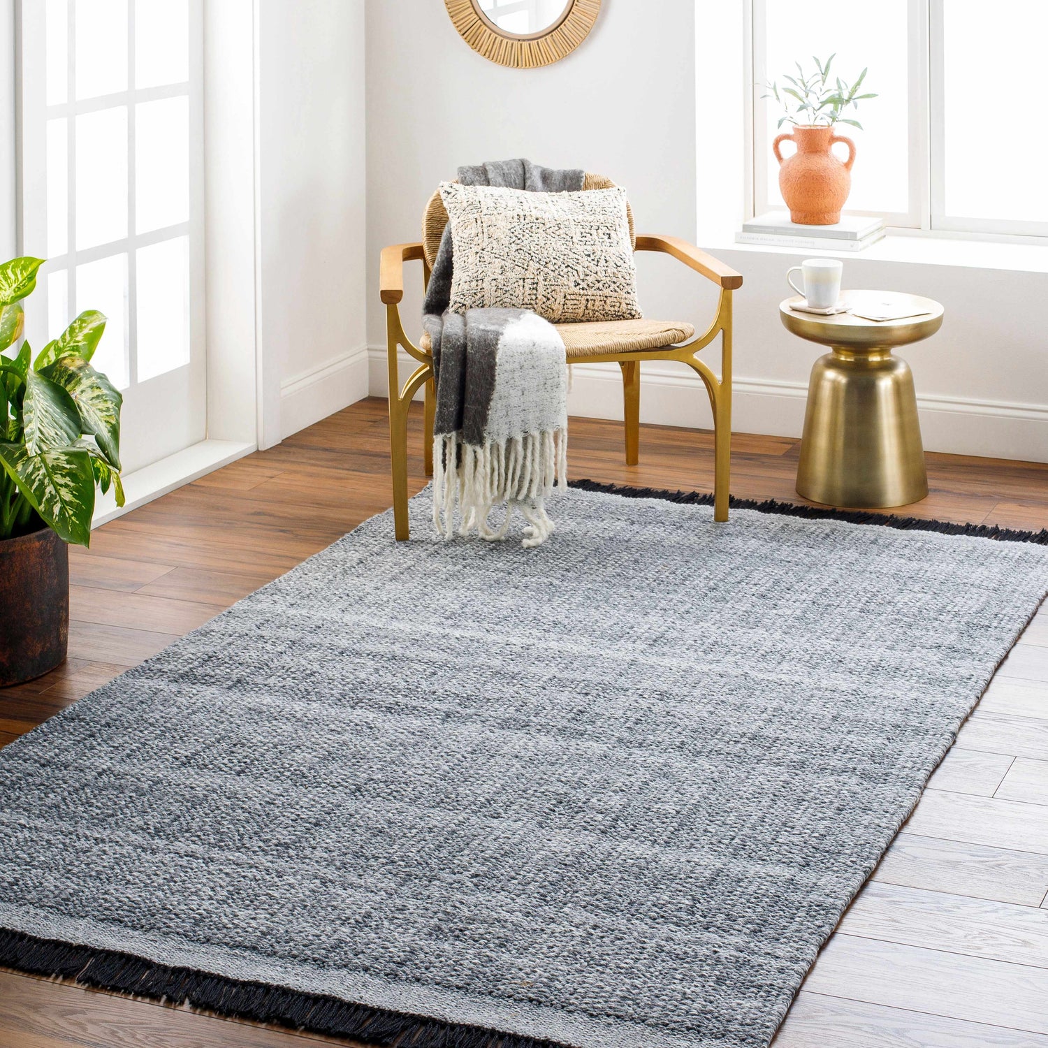 Living room scene with a dark gray Anane area rug, gold accent table, and chair with a throw. Roomscene-Rectangle