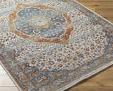 Close-up of the Bojan Area Rug in Beachhouse. Features traditional floral patterns in blue, brown, and copper tones. Corner