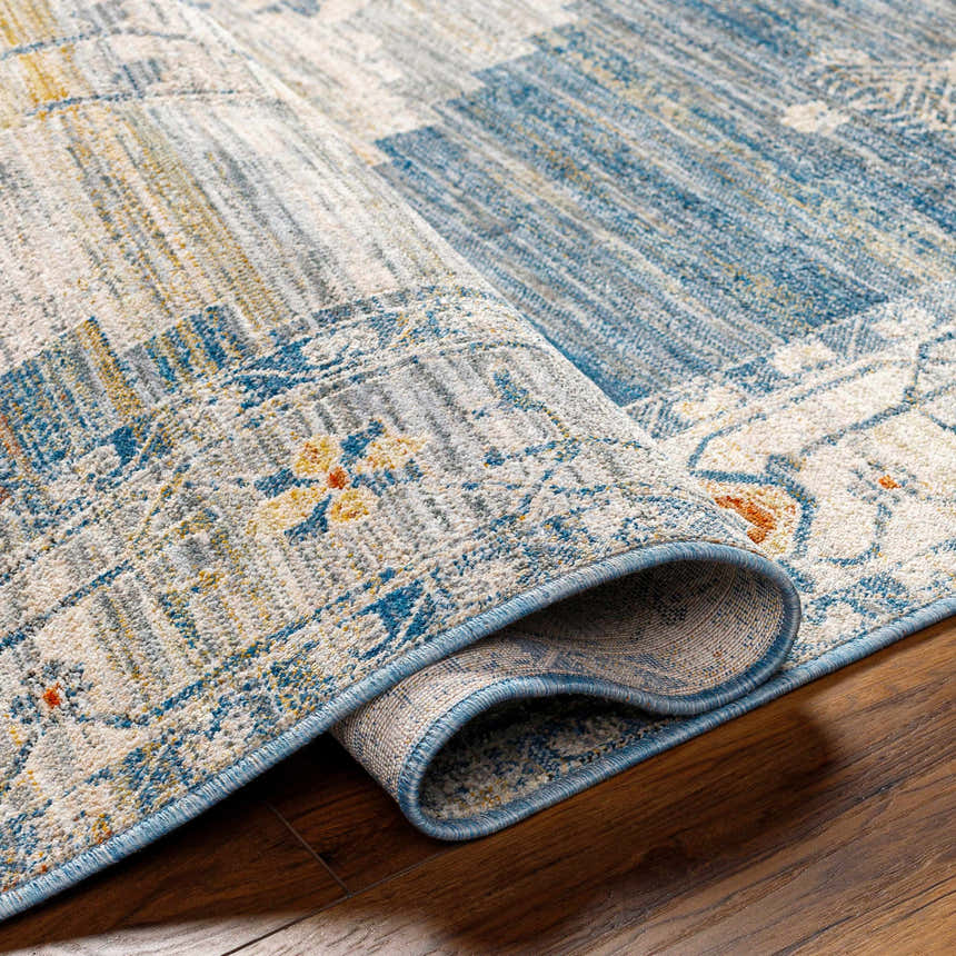 Close-up of the Shin Area Rug, a machine-woven rug in clay, copper, denim, and gray, with a traditional pattern. Fold