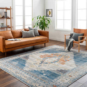 Living room scene with a Shin Area Rug in clay, copper, and denim colors, styled with a leather sofa and wood chair. Roomscene-Rectangle
