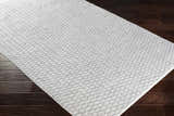 Close-up of the hand woven Scarborough Area Carpet. Gray and white rug with a subtle geometric pattern. Corner