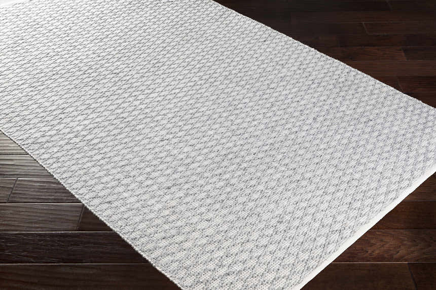 Close-up of the hand woven Scarborough Area Carpet. Gray and white rug with a subtle geometric pattern. Corner