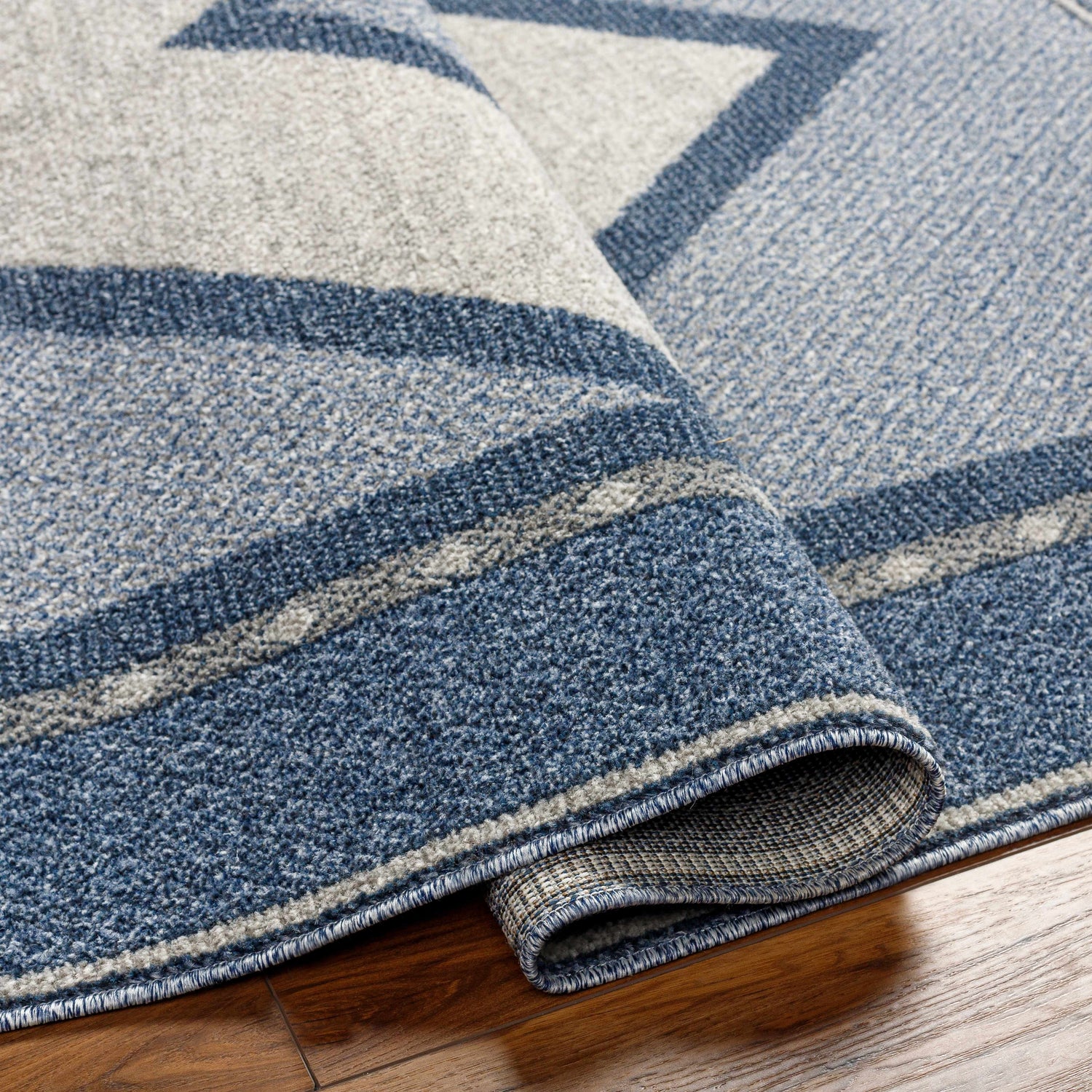 Close-up of the Onan Area Rug showing its arctic sky, gray, and silver geometric pattern and machine-woven texture. Fold