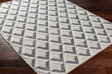 Close-up of the Maik Area Rug. Hand-woven geometric design in dark gray and light gray on a dark wood floor. Corner