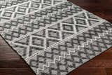 Close-up of the hand woven Yuka Area Rug. Dark gray and natural gray geometric pattern on recycled PET yarn. Corner