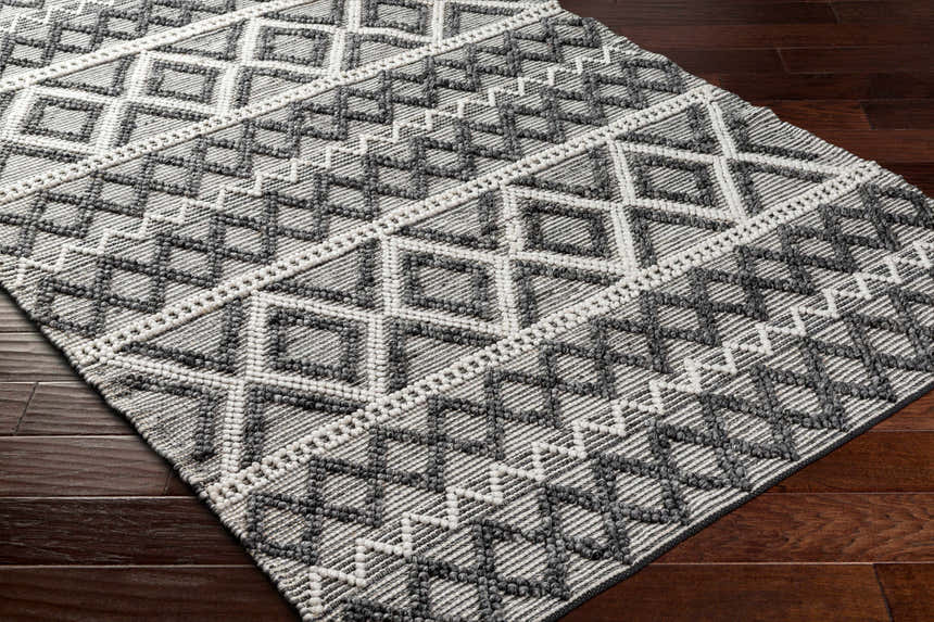 Close-up of the hand woven Yuka Area Rug. Dark gray and natural gray geometric pattern on recycled PET yarn. Corner