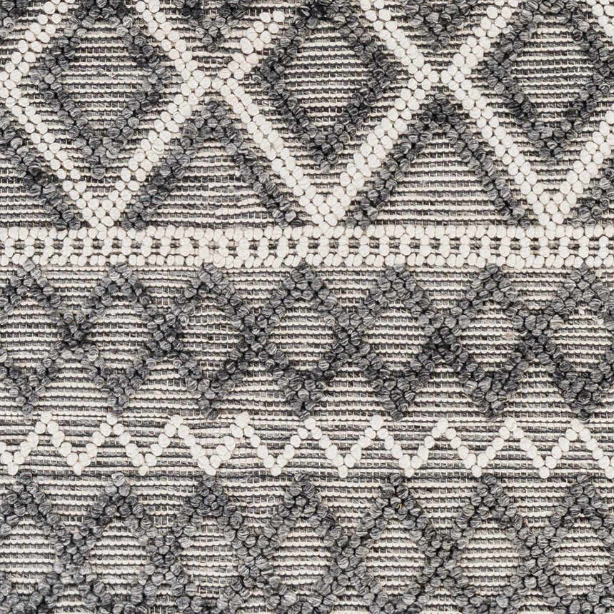 Close-up of the hand-woven Yuka Area Rug. Dark gray and natural gray geometric diamond pattern with textured recycled PET yarn. Swatch