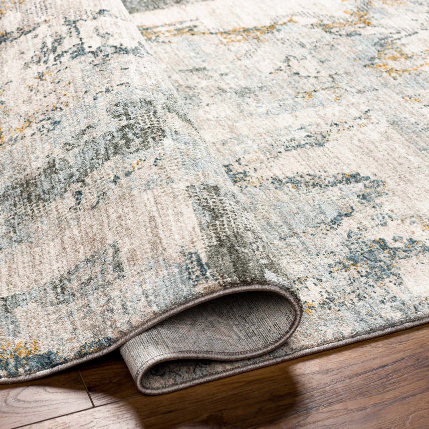 Close-up of the textured Adlai Rug with Fringes, showing its abstract pattern in dusty sage, ink blue, and off-white. Fold