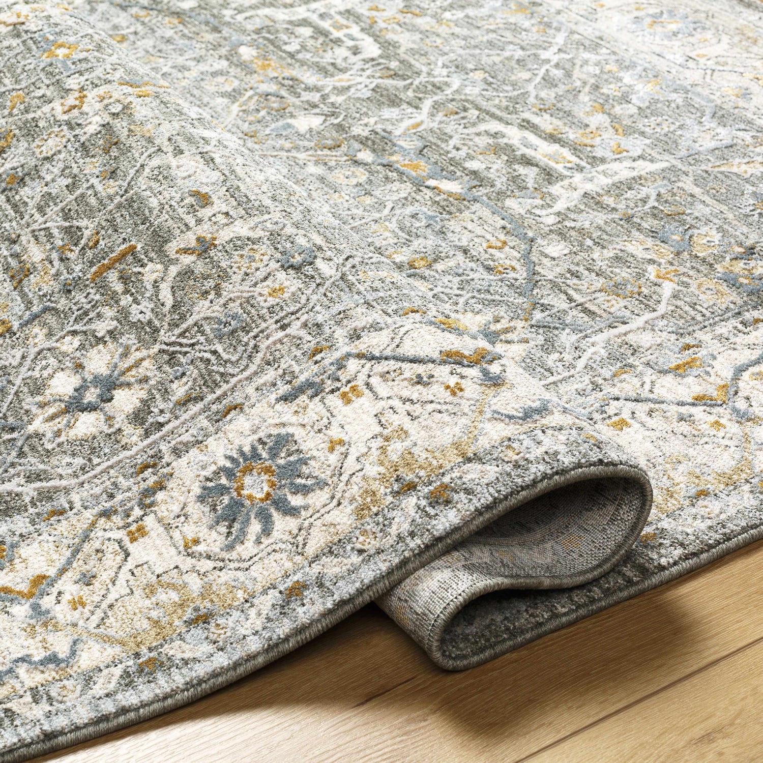 Close-up of textured Aviva Teal Rug. Features dusty sage, light gray, mustard, and off-white traditional pattern. Fold