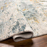 Close-up of the Chaya Textured Abstract Rug, showing its dusty sage, ink blue, and mustard colors, plus textured design. Fold