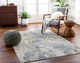 Living room scene with Chaya Textured Abstract Rug. Dusty sage, ink blue, and mustard accents complement the gray chair and wood furniture. Roomscene-Rectangle