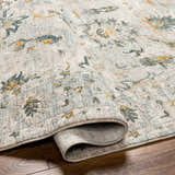 Close-up of the Emile Textured Rug. Features a traditional pattern in dusty sage, light gray, mustard, and off-white. Fold