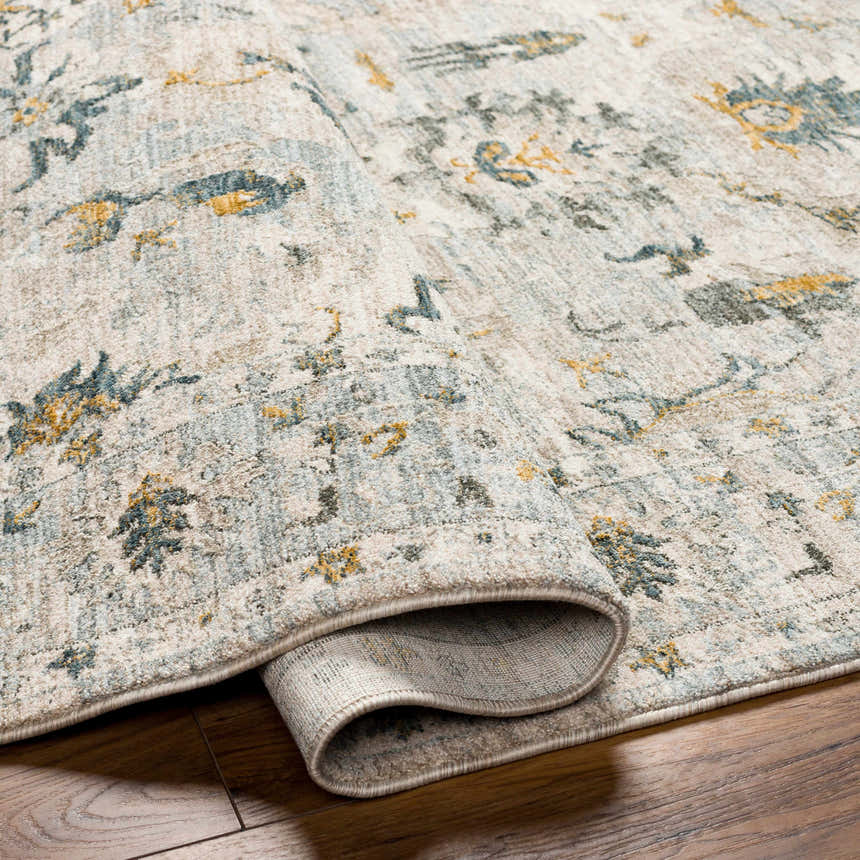 Close-up of the Emile Textured Rug. Features a traditional pattern in dusty sage, light gray, mustard, and off-white. Fold