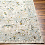 Close-up of the Emile Textured Rug. Features a traditional design in dusty sage, light gray, and mustard on a wood floor. Front