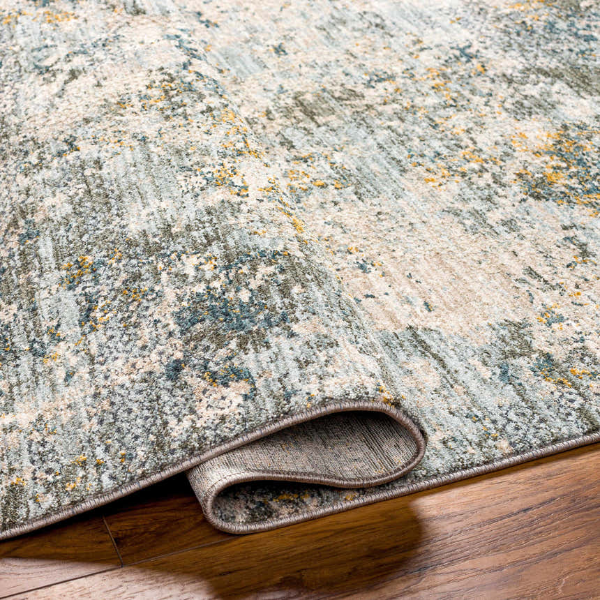 Close-up of the Pizi Textured Rug with Fringes in dusty sage, ink blue, and mustard on a wood floor. Contemporary style. Fold