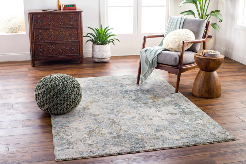 Living room scene with Pizi Textured Rug, gray chair, wood accents, and sage green pouf on a wood floor. Roomscene-Rectangle