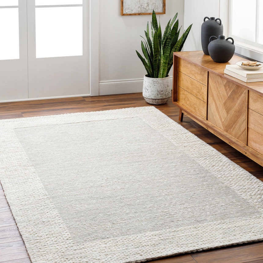 Living room scene with a Jojen Off White Jute Area Rug, wood floors, and a light wood cabinet with black vases. Roomscene-Rectangle