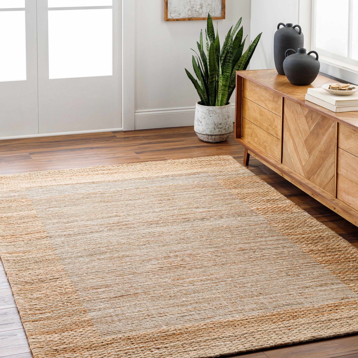 Living room scene with a lambswool and light brown Jojen Jute Area Rug, wood floors, and a mid-century modern cabinet. Roomscene-Rectangle