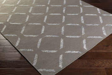 Close-up of the Seeley Area Carpet. Brown rug with off-white geometric square pattern on dark wood floor. Corner