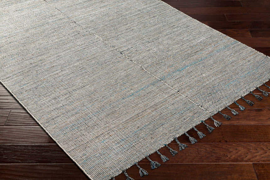 Close-up of Anaya Beige & Teal Area Rug showing woven texture, teal accents, and tassels on dark wood floor. Corner