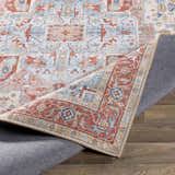 Close-up of the Selbyville Area Rug showing brick red, light blue, and ivory oriental pattern and the rug's backing. Fold