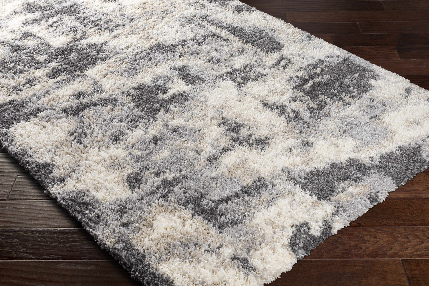 Close up of the Selcuklu Area Rug, a shag rug in black, cream, beige, and gray on dark wood floors. Corner