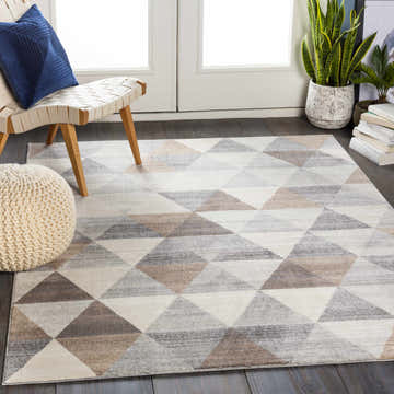 Living room scene with a Sells Gray&Brown Triangles Area Carpet, chair, blue pillow, and knit ottoman. Roomscene-Rectangle