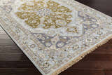 Close-up of the Senath Area Rug in ivory, olive, and mauve on a dark wood floor, showing its traditional pattern and fringe. Corner