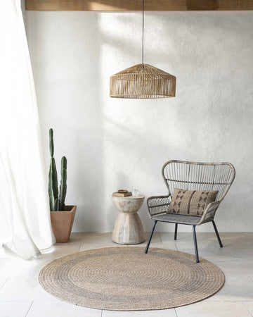 Light and airy room featuring a round Andie Bordered Faux Jute Rug, woven chair, side table, and cactus. Roomscene-Round
