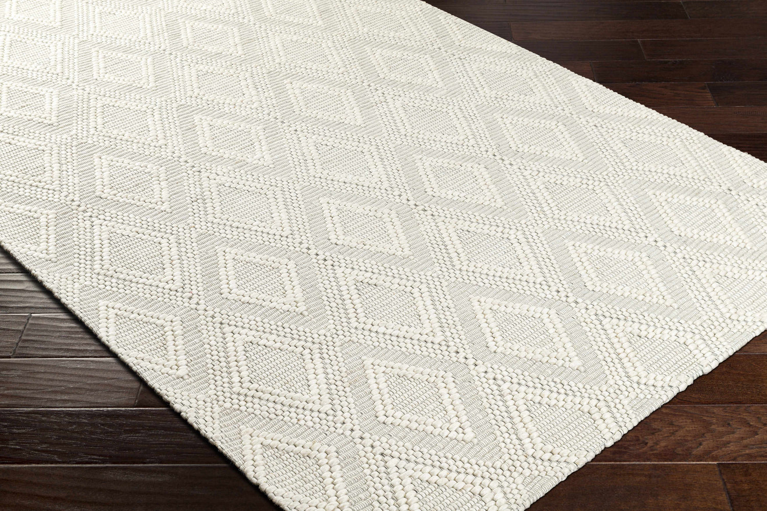 Close-up of the hand woven Kasib Cream Area Rug showcasing its diamond pattern and textured weave on a dark wood floor. Corner
