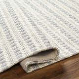 Close-up of the hand-woven Laleh Gray Area Rug showing its beige and rose cream geometric pattern and wool texture. Fold