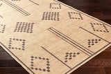 Close-up of the Fathi Washable Area Rug. Tan rug with dark brown geometric shapes and lines on dark wood flooring. Corner