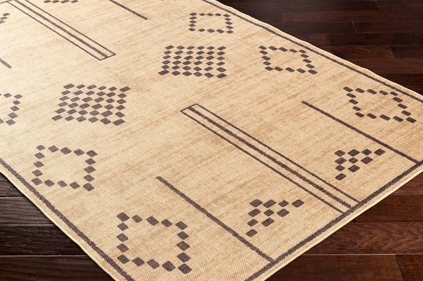 Close-up of the Fathi Washable Area Rug. Tan rug with dark brown geometric shapes and lines on dark wood flooring. Corner