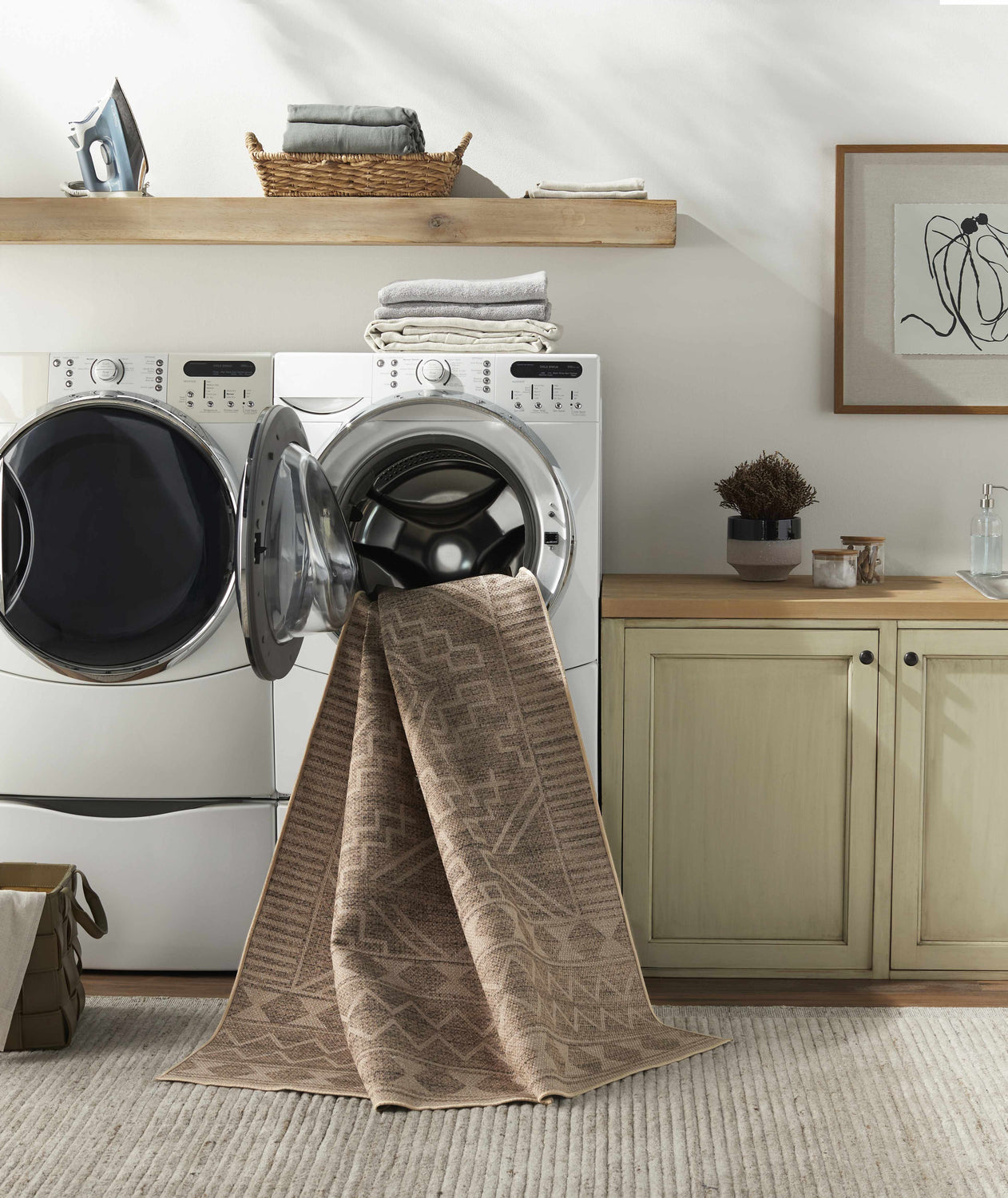 Laundry room with Halle Beige Washable Area Rug draped from the dryer, showcasing its brown geometric pattern. Washing-Machine