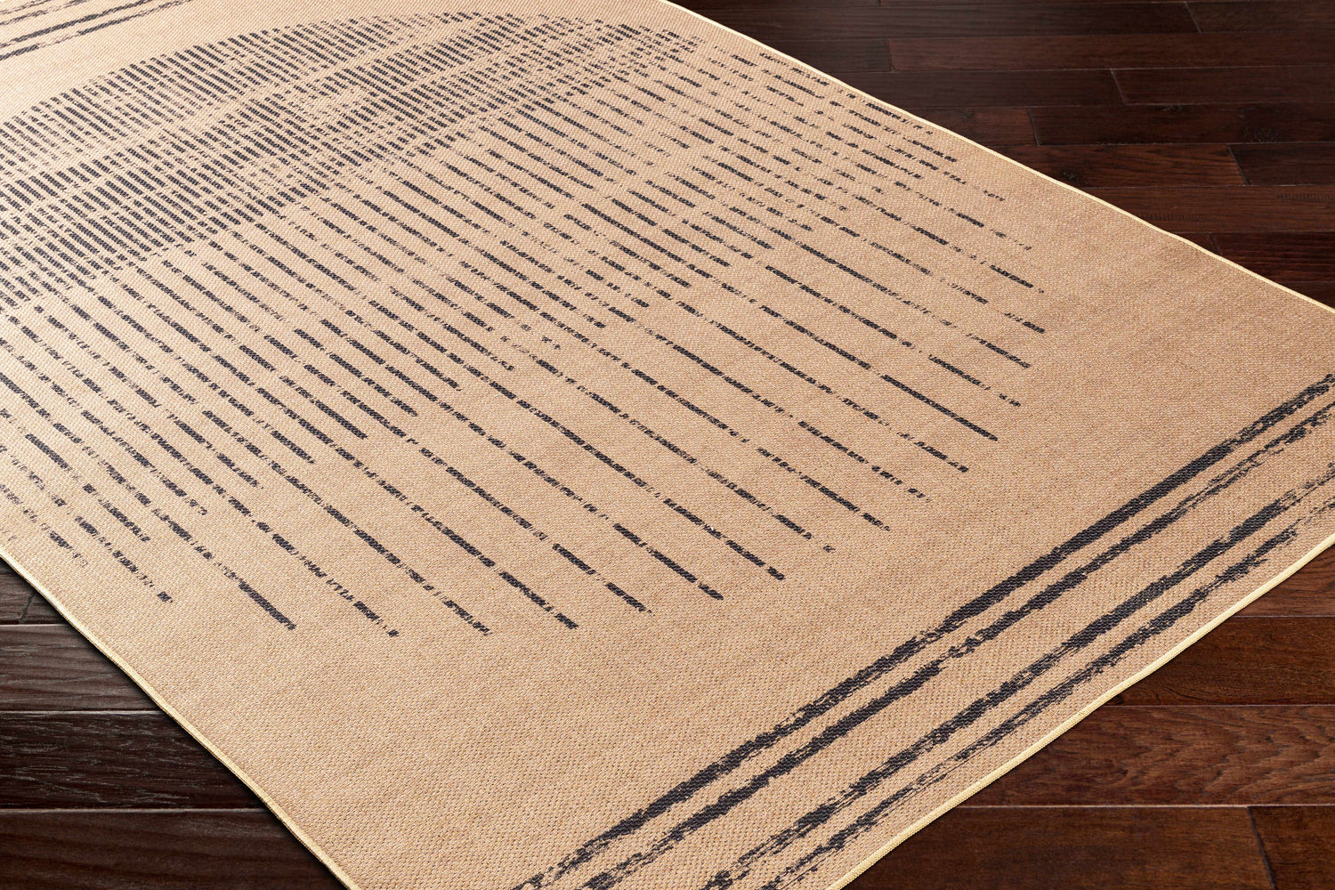 Close-up of the Yuki Washable Area Rug in camel with dark brown linear pattern on dark wood floor. Farmhouse style. Corner