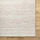 Close-up of the hand-tufted Urmat Wool Area Rug in light silver, pearl, and warm gray on a wood floor. Corner