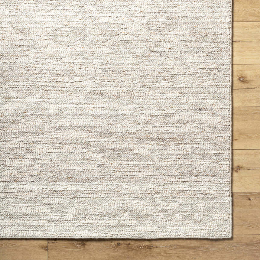 Close-up of the hand-tufted Urmat Wool Area Rug in light silver, pearl, and warm gray on a wood floor. Corner